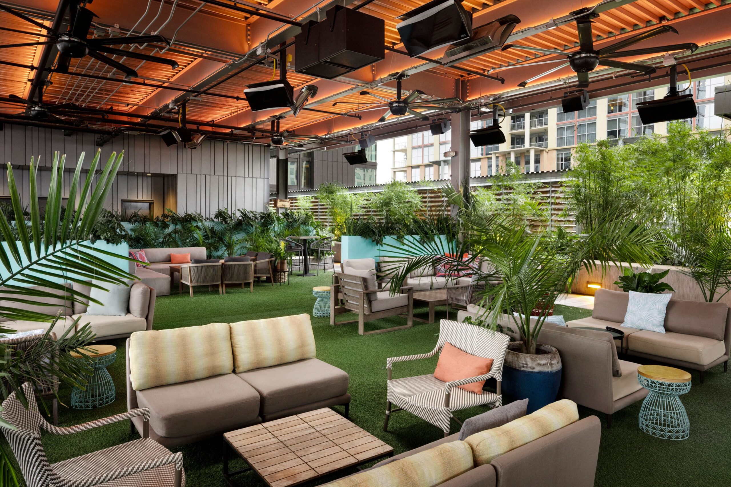 Photo of Zanzibar rooftop lounge in Austin, TX, showcasing a tropical-inspired setting with cushioned seating, palm plants, turf flooring, and warm ambient lighting—ideal for casual networking and events.